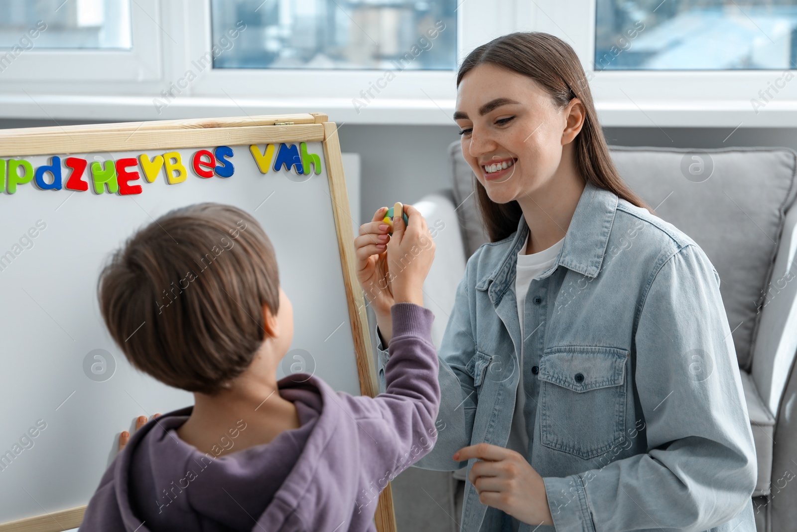 Photo of Speech therapist teaching little boy alphabet with magnetic letters indoors