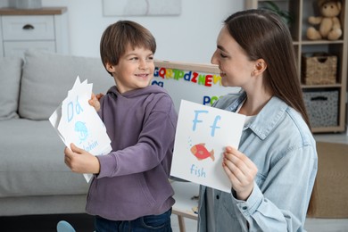 Photo of Speech therapist teaching little boy alphabet with different pictures indoors