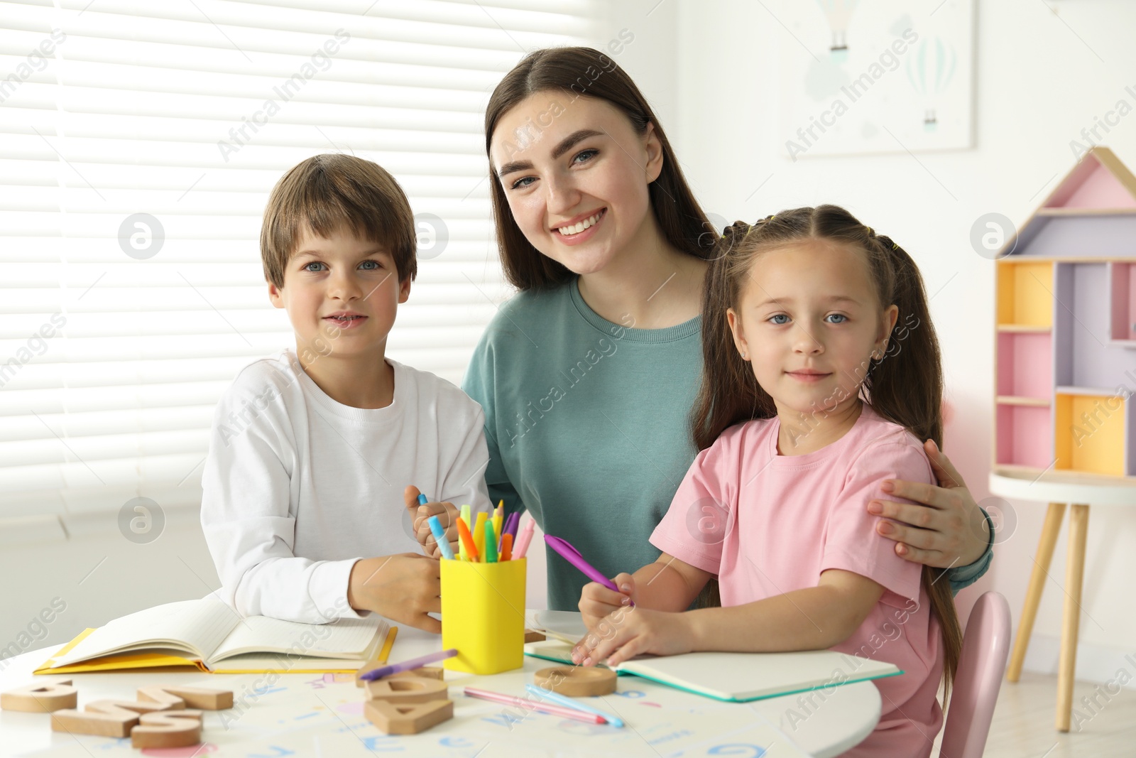 Photo of Speech therapist teaching little kids alphabet at white table indoors