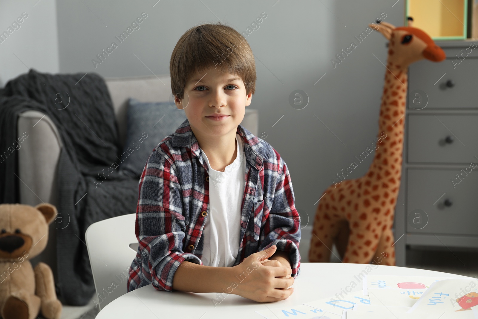 Photo of Learning alphabet. Little boy at white table with different pictures indoors