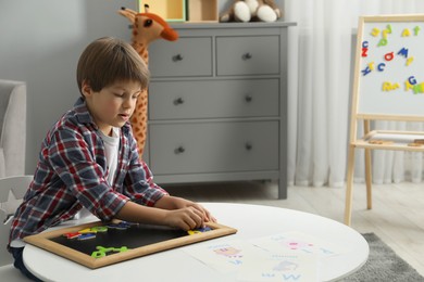 Photo of Little boy learning alphabet with magnetic letters at white table indoors