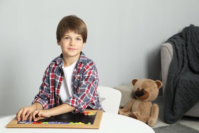 Photo of Little boy learning alphabet with magnetic letters at white table indoors