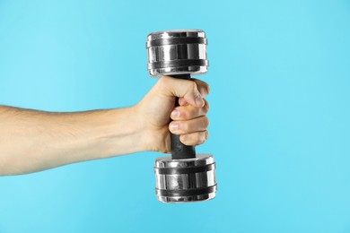 Man exercising with dumbbell on light blue background, closeup