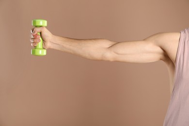 Photo of Man exercising with dumbbell on light brown background, closeup