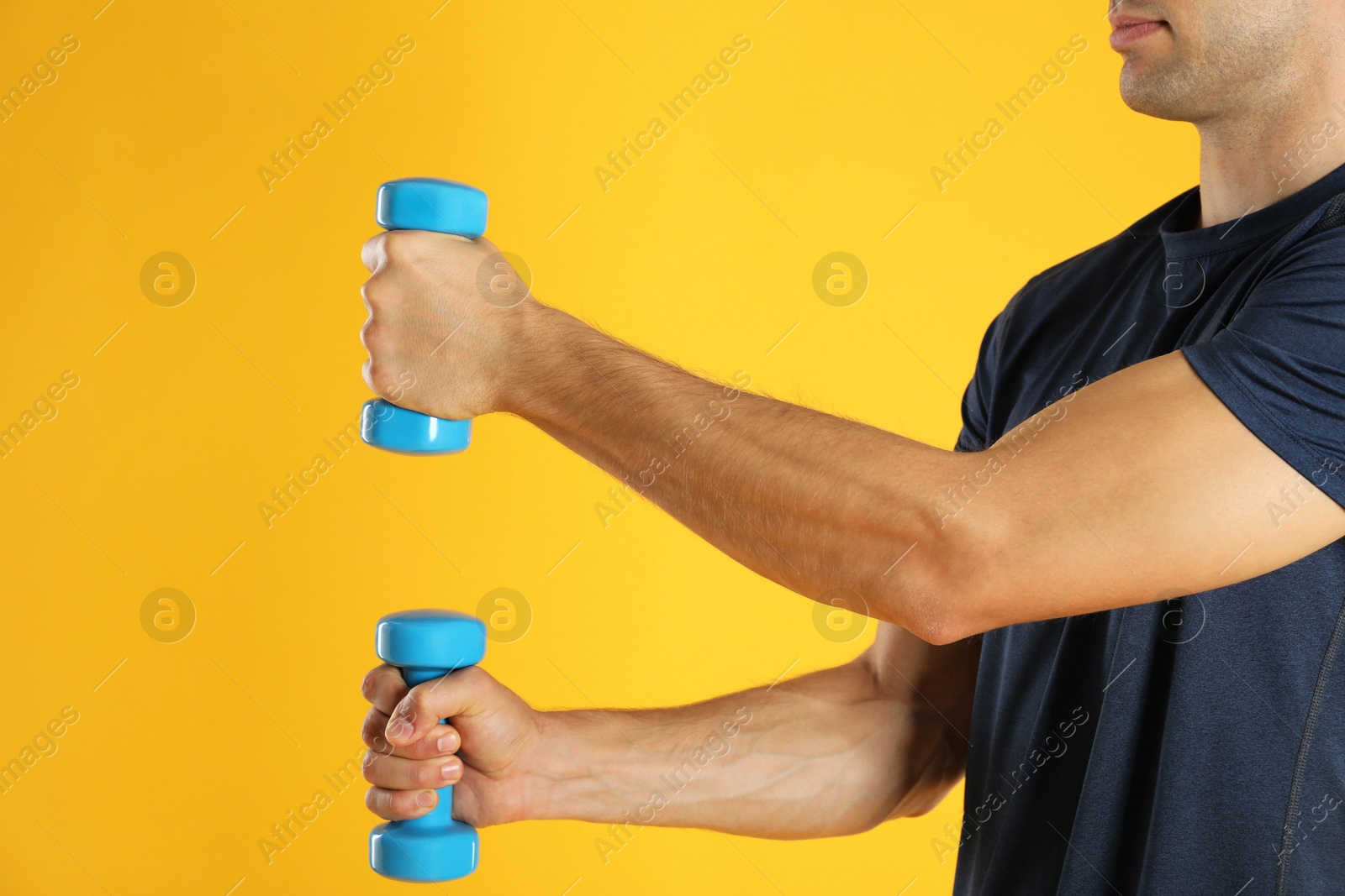 Photo of Man exercising with dumbbells on yellow background, closeup