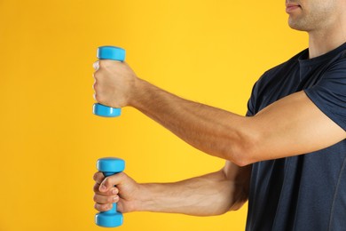 Photo of Man exercising with dumbbells on yellow background, closeup