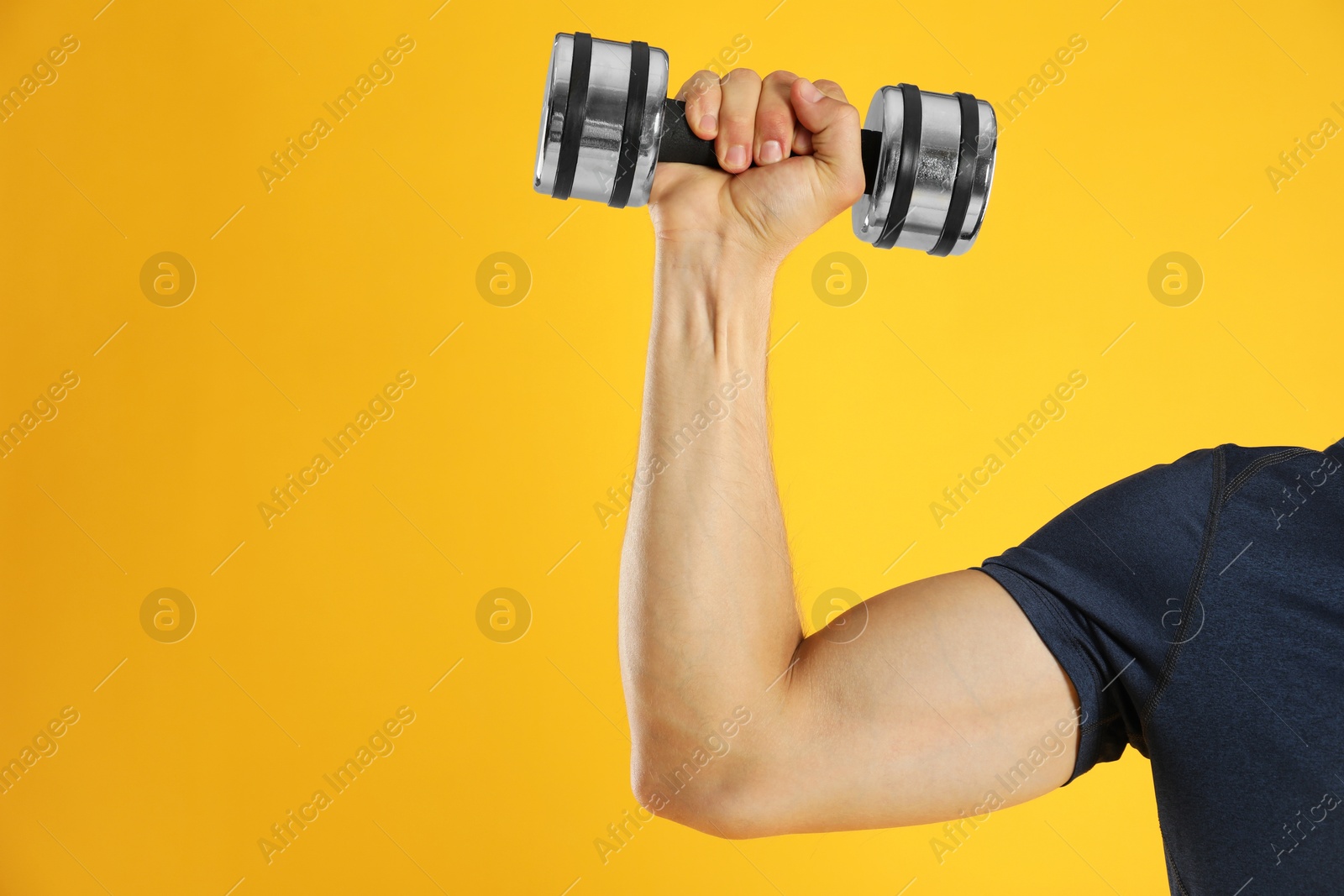 Photo of Man exercising with dumbbell on yellow background, closeup. Space for text