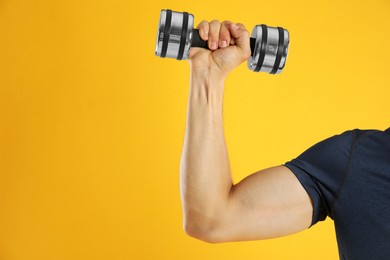 Photo of Man exercising with dumbbell on yellow background, closeup. Space for text