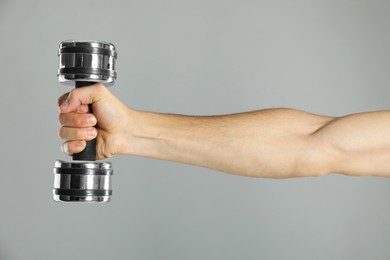 Photo of Man exercising with dumbbell on grey background, closeup