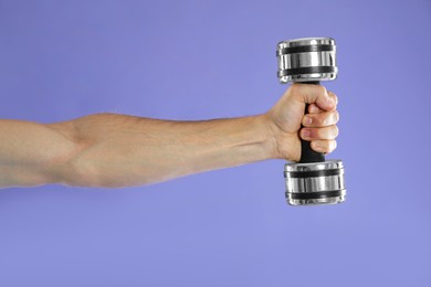 Photo of Man exercising with dumbbell on violet background, closeup