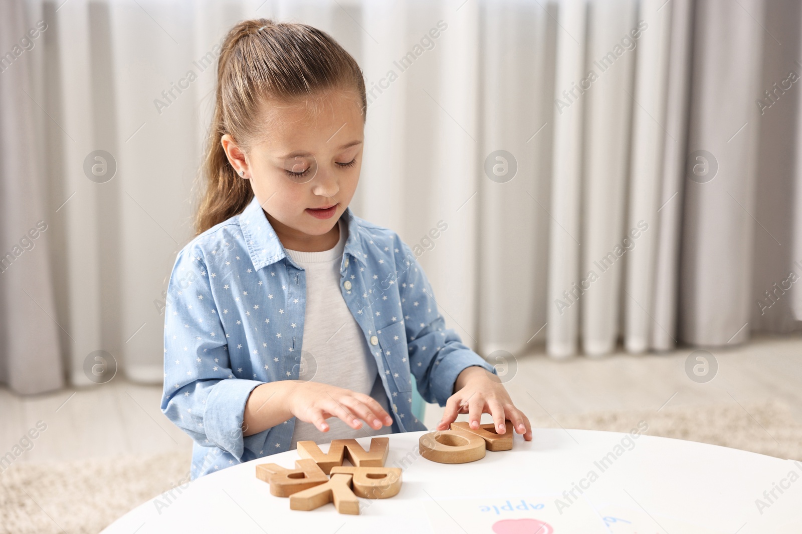 Photo of Little girl learning alphabet with wooden letters at white table indoors, space for text