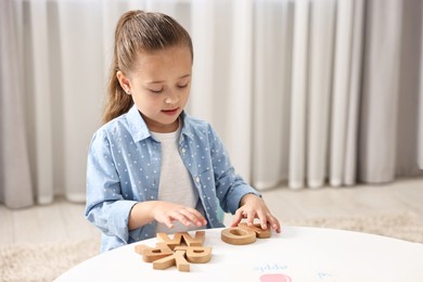 Photo of Little girl learning alphabet with wooden letters at white table indoors, space for text