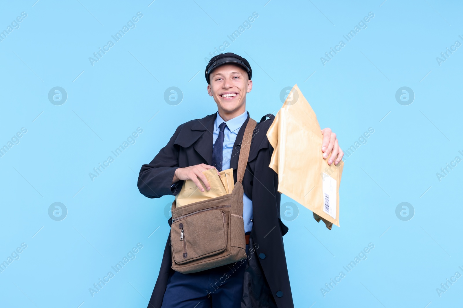 Photo of Happy postman with bag giving envelopes on light blue background