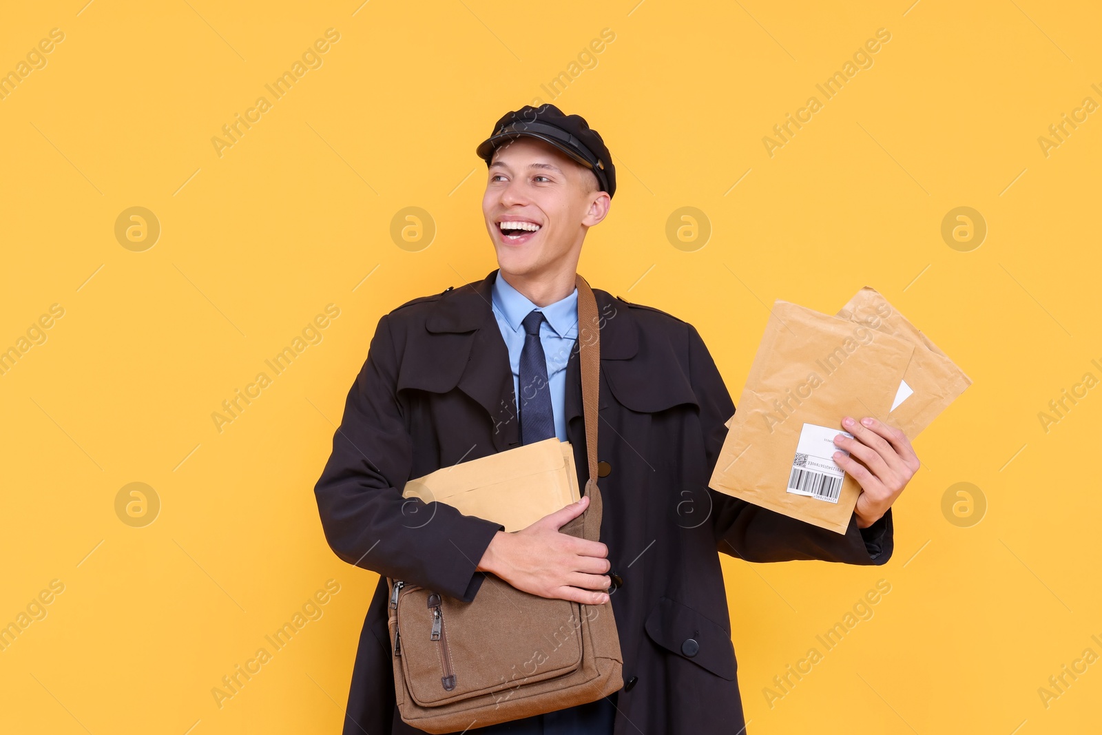 Photo of Happy postman with bag and envelopes on yellow background. Space for text