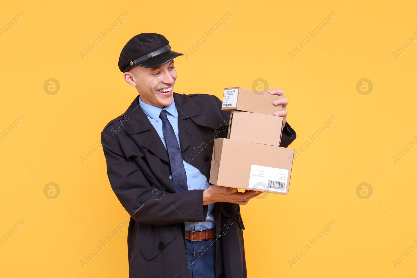 Photo of Happy postman with parcels on yellow background