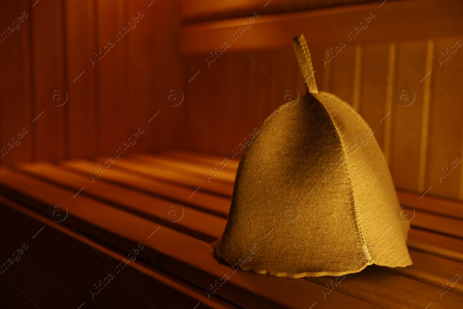 Photo of Felt wool hat on wooden bench in sauna. Space for text