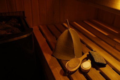 Photo of Felt wool hat and bath accessories on wooden bench in sauna