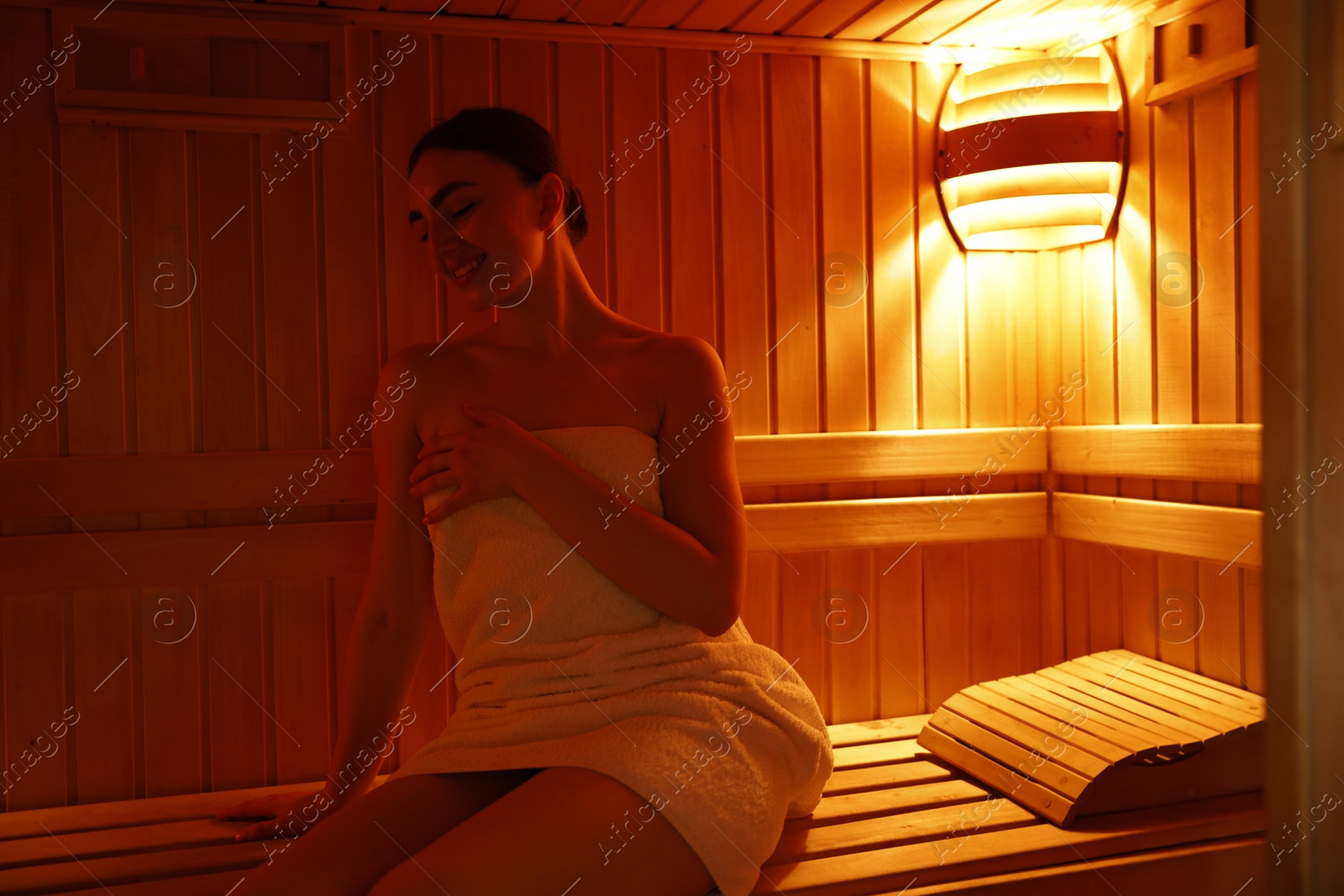 Photo of Beautiful woman wrapped in towel on bench at sauna