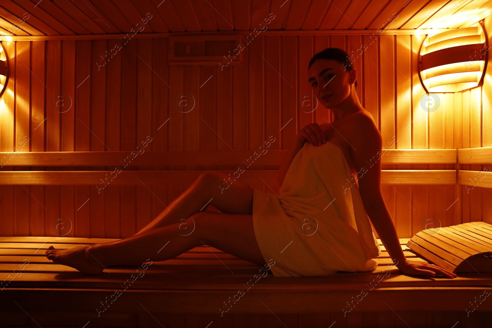 Photo of Beautiful woman wrapped in towel on bench at sauna