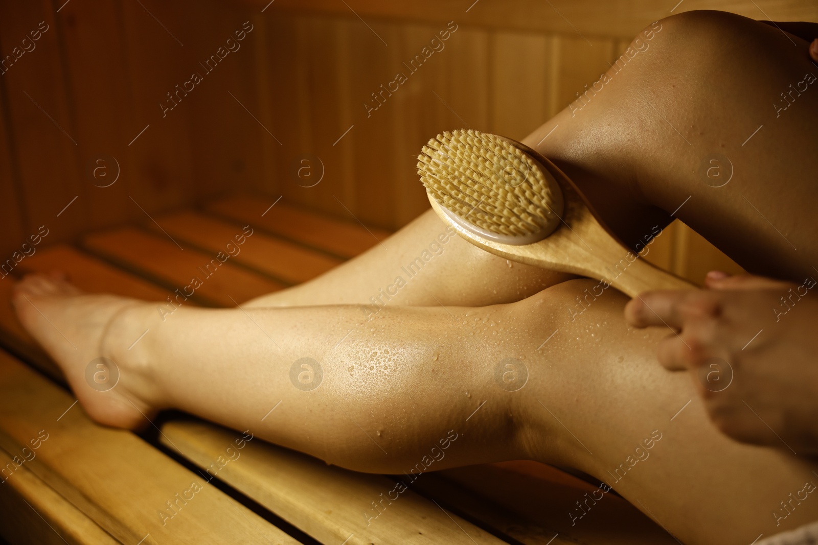 Photo of Woman with massage brush on bench in sauna, closeup