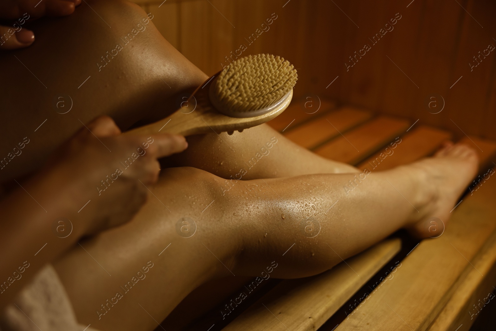 Photo of Woman with massage brush on bench in sauna, closeup