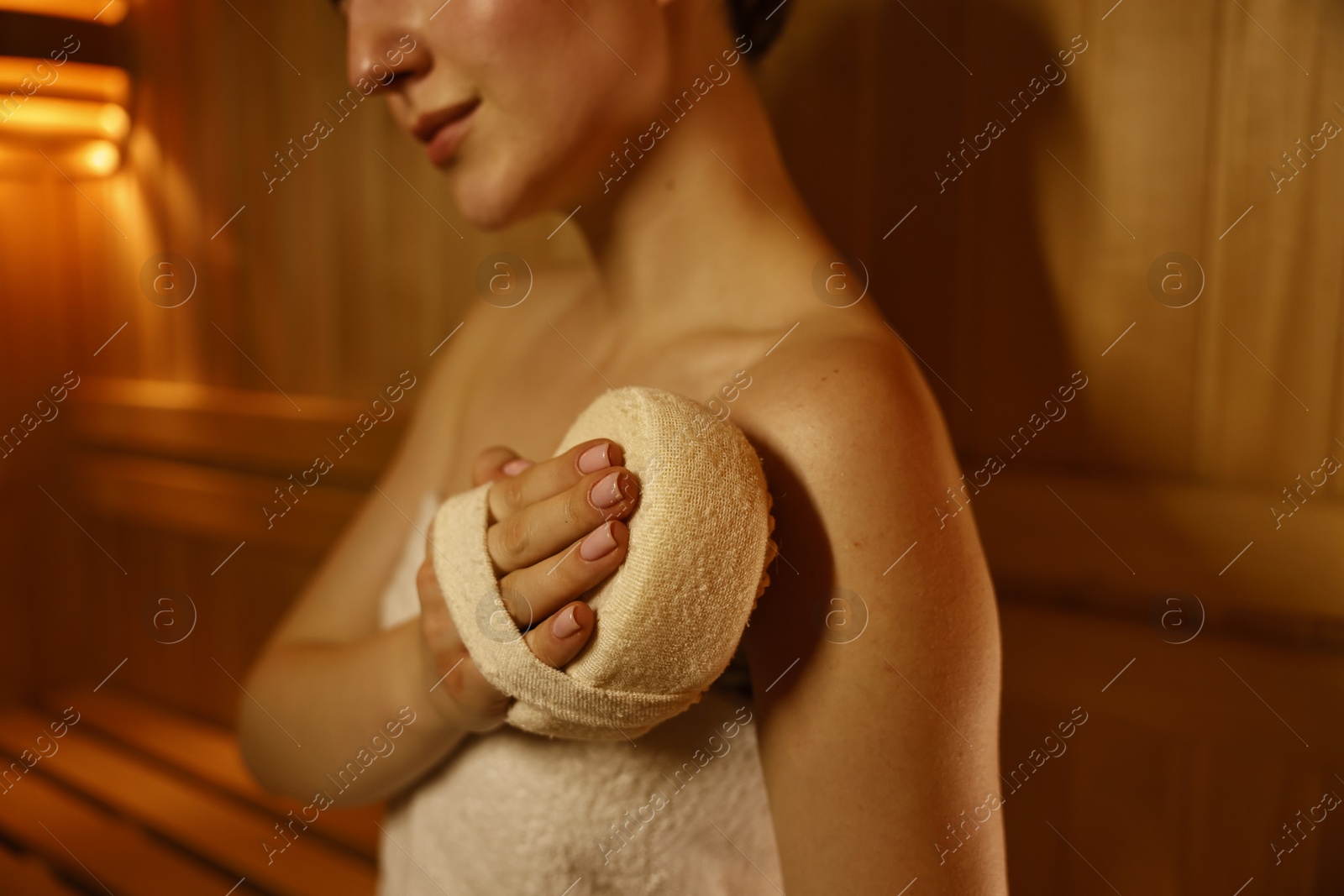 Photo of Woman with massage sponge in sauna, closeup