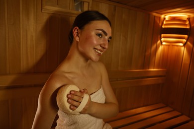 Photo of Smiling woman with massage sponge in sauna