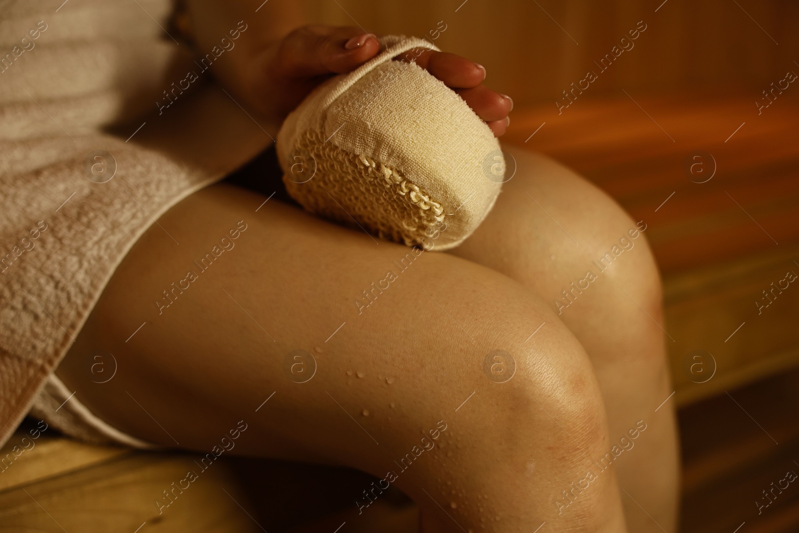 Photo of Woman with massage sponge on bench in sauna, closeup