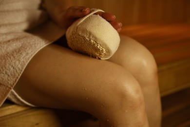 Photo of Woman with massage sponge on bench in sauna, closeup