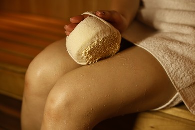 Photo of Woman with massage sponge on bench in sauna, closeup