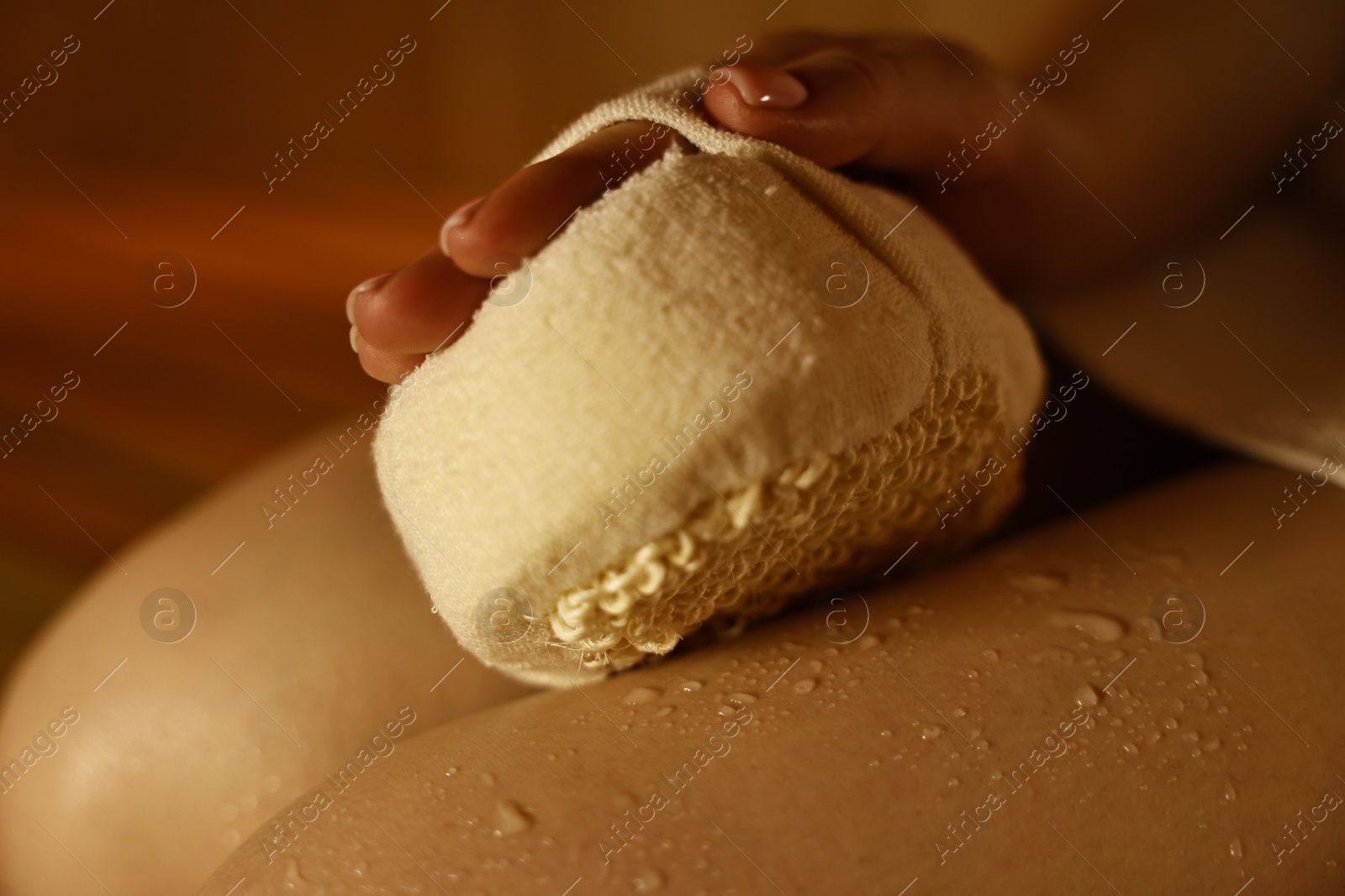 Photo of Woman with massage sponge on bench in sauna, closeup