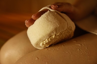 Photo of Woman with massage sponge on bench in sauna, closeup