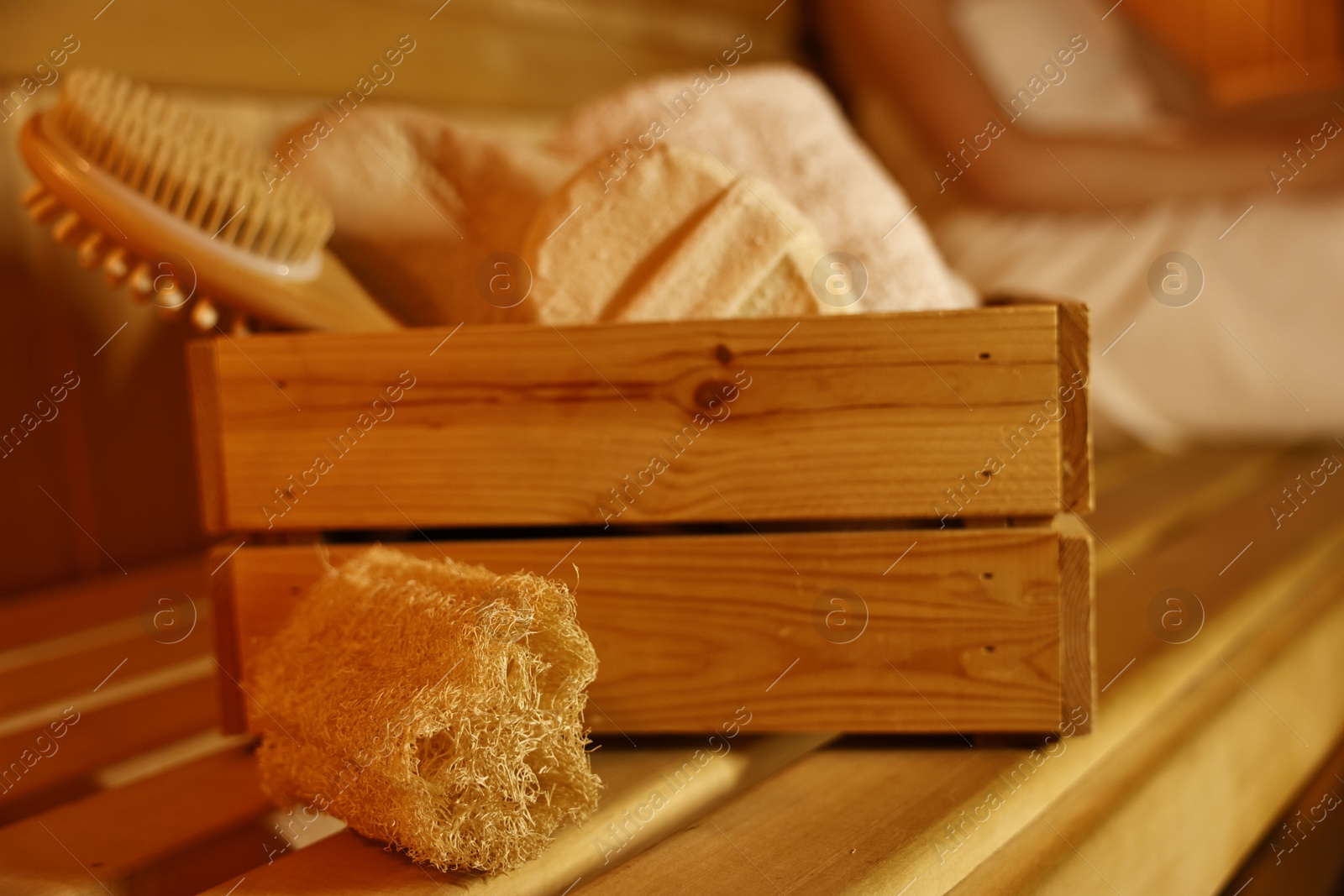 Photo of Crate with bath accessories and woman on wooden bench in sauna, selective focus