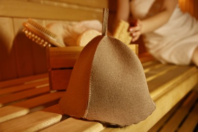 Photo of Woman with bath accessories and felt wool hat on wooden bench in sauna, selective focus