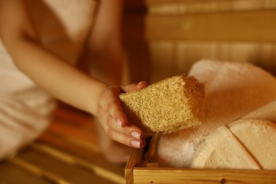 Photo of Woman with bath accessories on wooden bench in sauna, closeup