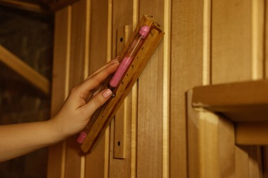 Photo of Woman turning hourglass on wooden wall in sauna, closeup