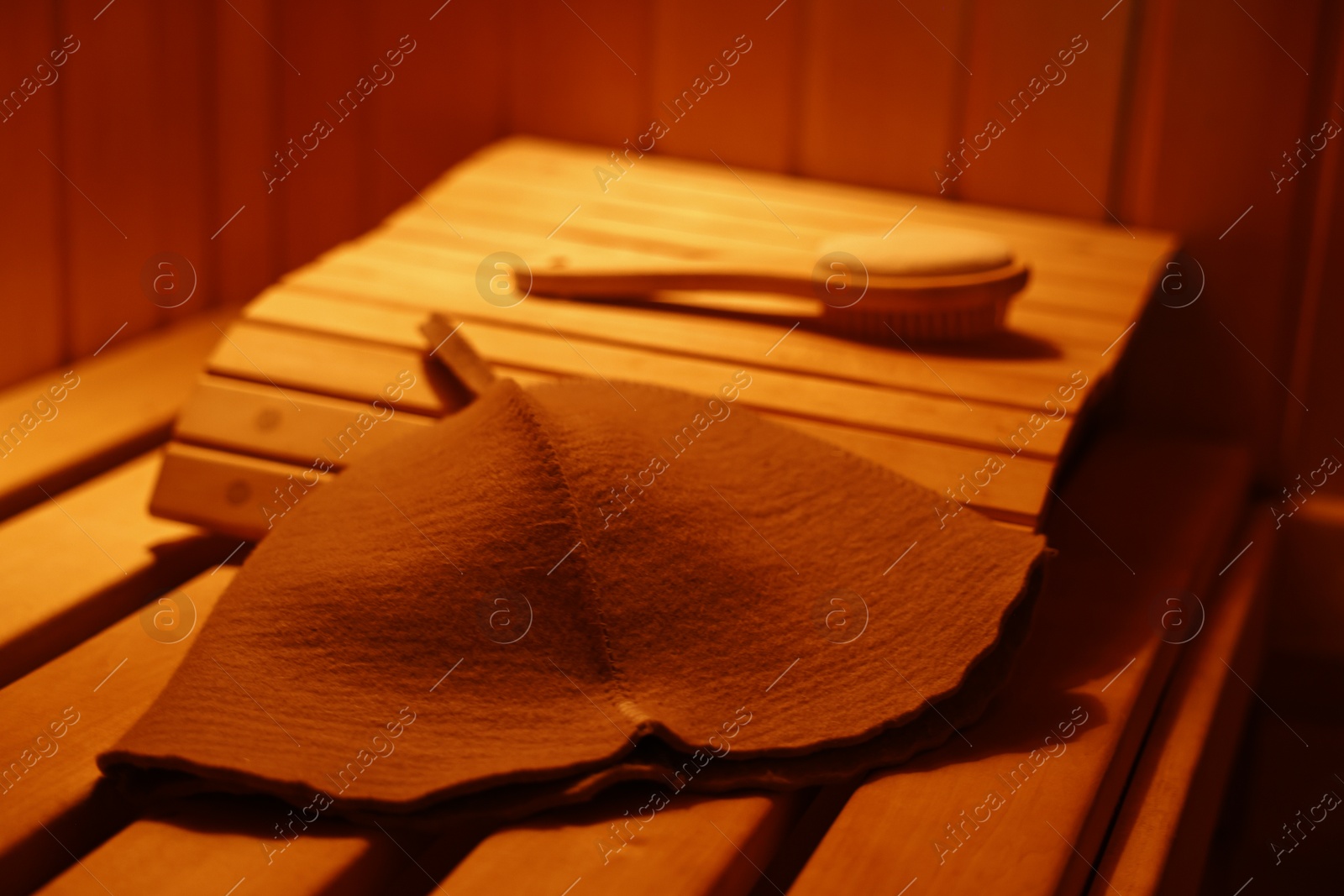 Photo of Felt wool hat and massage brush on wooden bench in sauna