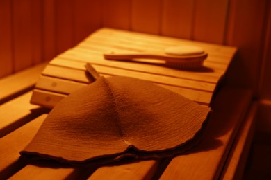 Photo of Felt wool hat and massage brush on wooden bench in sauna