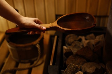 Photo of Woman pouring water on stones in sauna, closeup