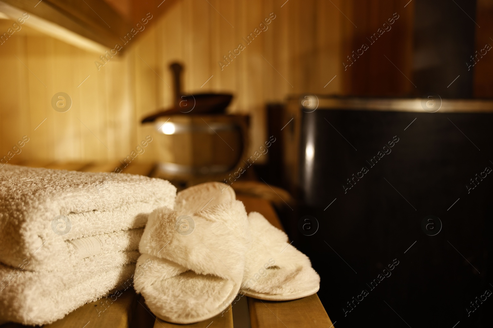 Photo of Towels and slippers on wooden bench in sauna