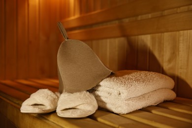 Photo of Felt wool hat, towels and slippers on wooden bench in sauna