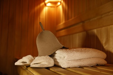 Photo of Felt wool hat, towels and slippers on wooden bench in sauna