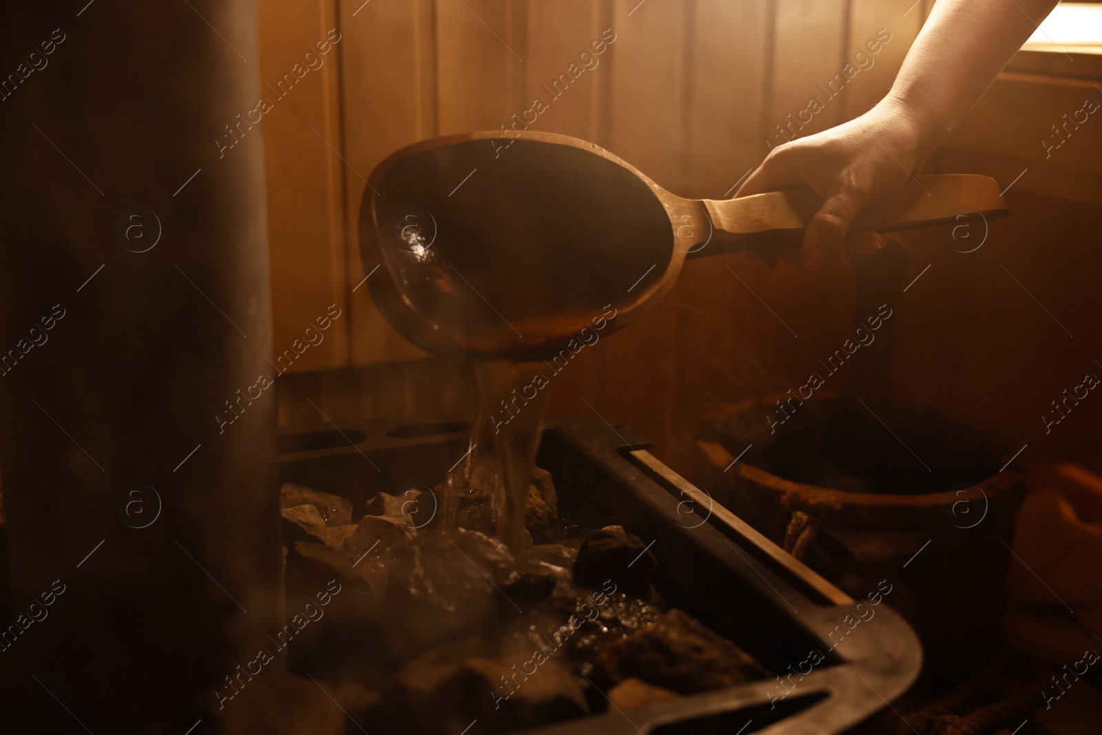 Photo of Woman pouring water on stones in sauna, closeup