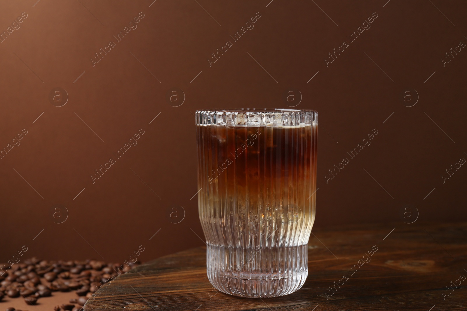 Photo of Refreshing espresso tonic drink on wooden table against brown background