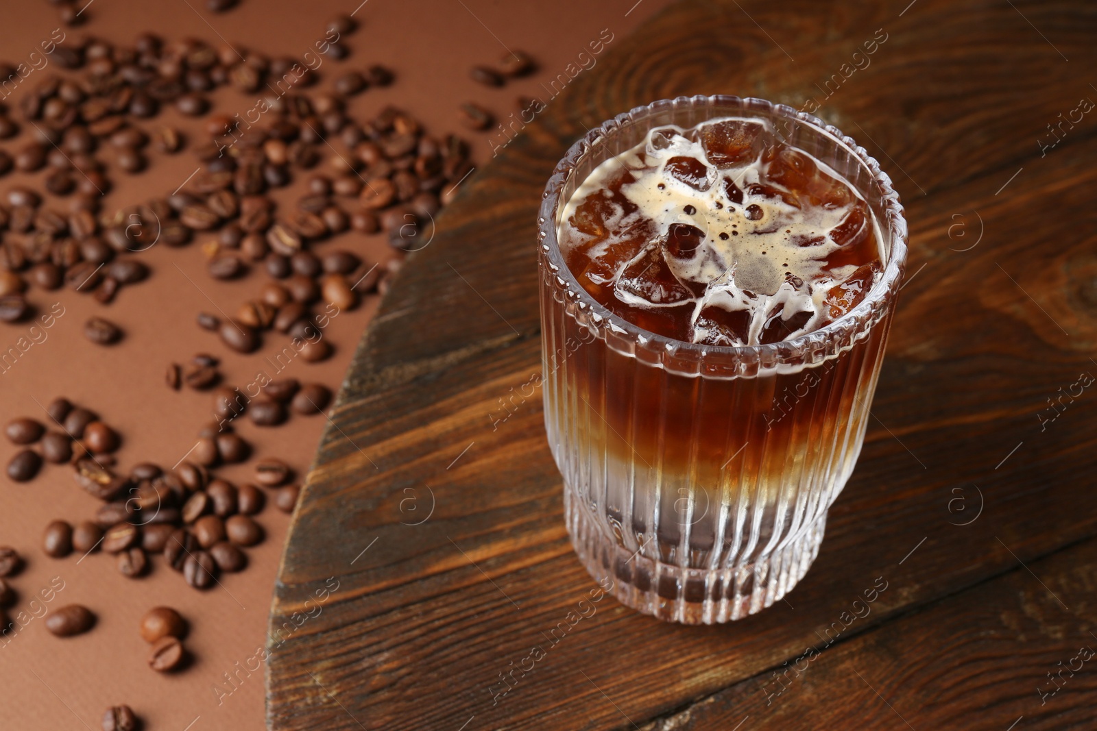 Photo of Refreshing espresso tonic drink and coffee beans on brown background, closeup