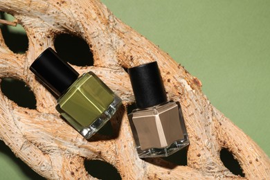 Photo of Nail polishes in bottles and piece of decorative wood on green background, top view