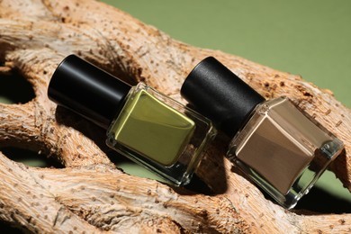 Photo of Nail polishes in bottles and piece of decorative wood on green background, closeup