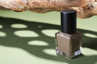 Photo of Nail polish in bottle and piece of decorative wood on green background, closeup