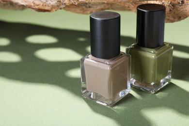 Photo of Nail polishes in bottles and piece of decorative wood on green background, closeup