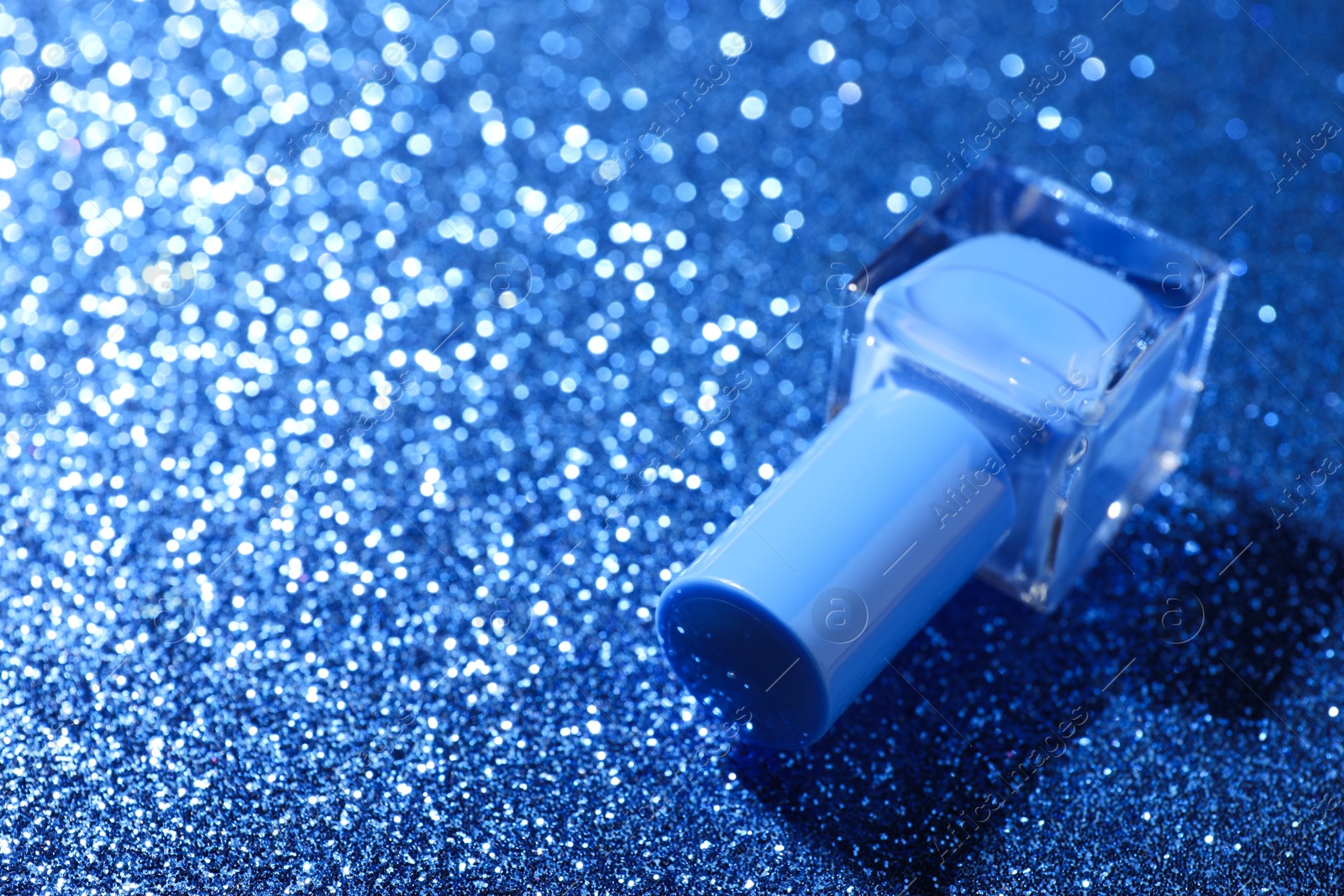 Photo of Nail polish in bottle on blue glitter surface, closeup. Space for text